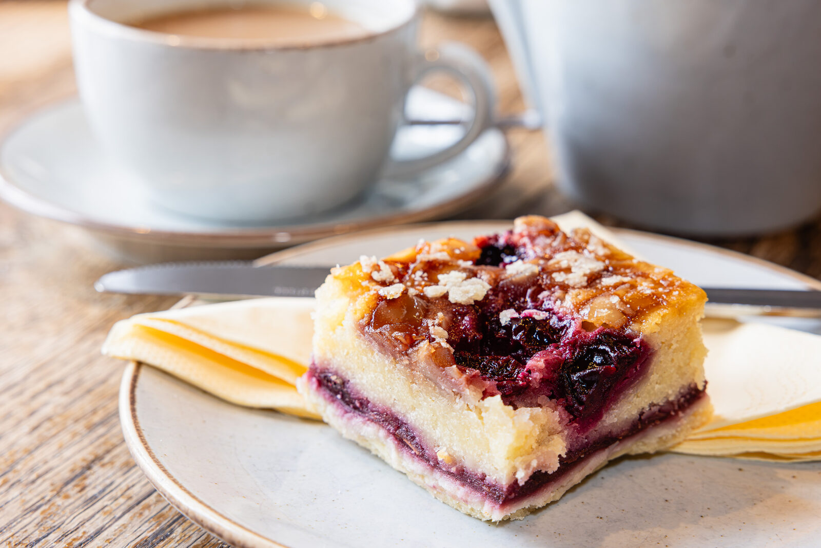 A berry bakewell tray-bake slice served with coffee